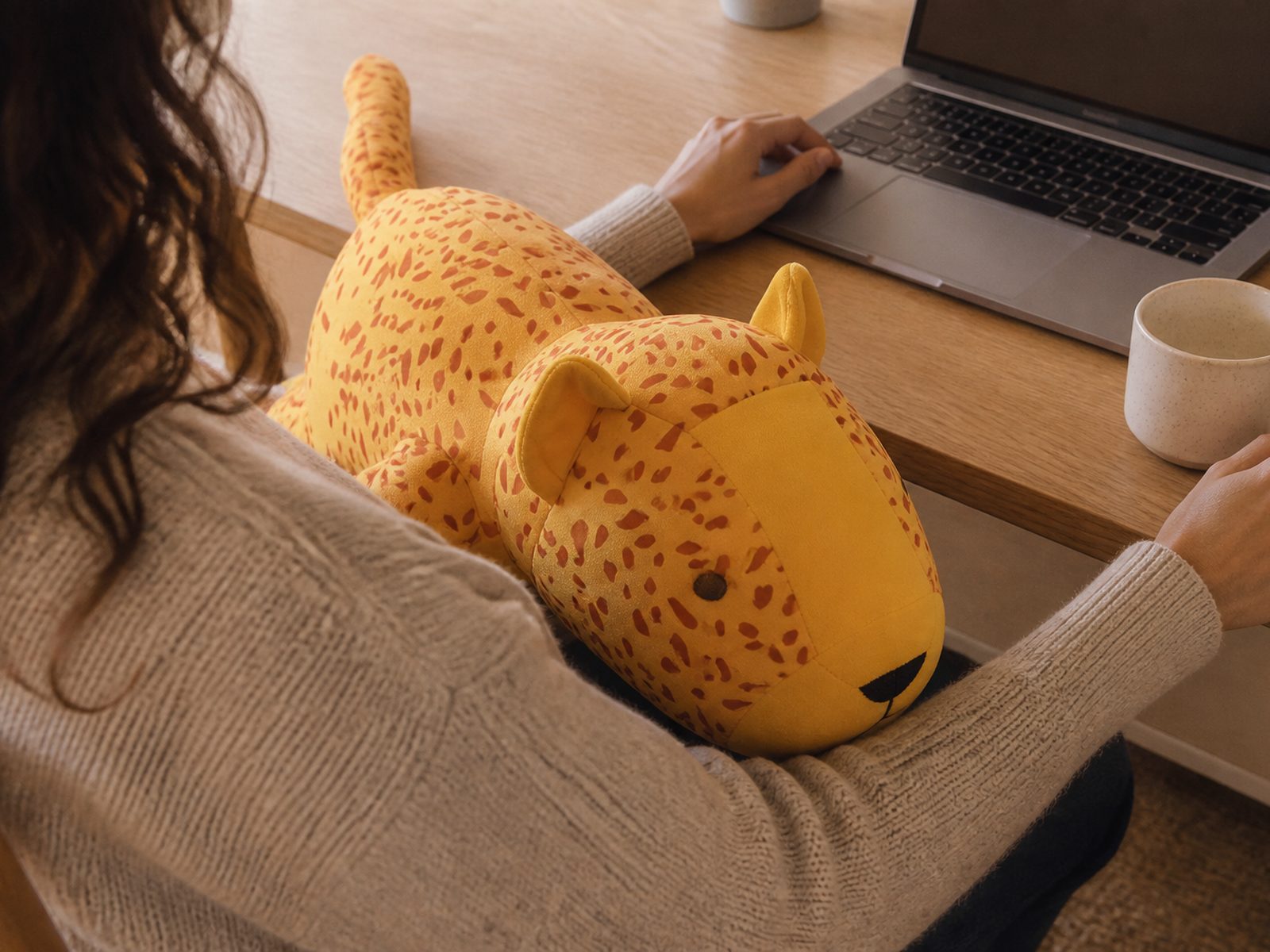 The yellow leopard weighted plushie sitting on someone's lap at a desk, their hands free to work